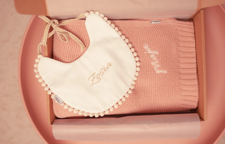 alt="Personalizowany zestaw prezentowy dla niemowlaka – kocyk i śliniaczek z imieniem dziecka. Idealny prezent na chrzest, baby shower lub narodziny, wyprawka dla noworodka z haftem."